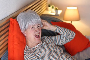 Olgun gri saçlı kadın evde yalnızlık çekerken yatakta yatıyor.