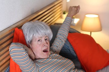 Olgun gri saçlı kadın evde yalnızlık çekerken yatakta geriniyor.