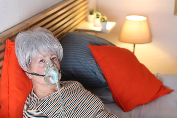 在家中自我隔离时 躺在床上休息时 戴着氧气面罩的成熟的灰发女人 — 图库照片