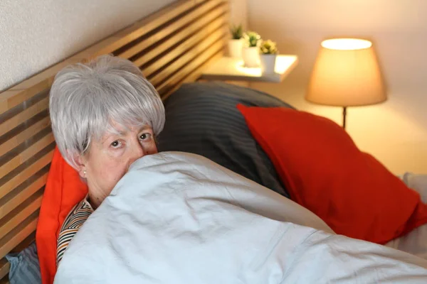 成熟的灰发女人在家里自我隔离时躺在床上休息时被毯子盖住 — 图库照片