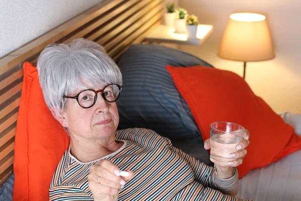 成熟した白髪の女性は薬を飲みながら家での隔離中にベッドでリラックスして — ストック写真