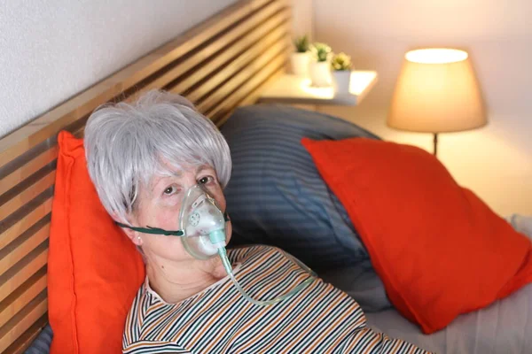 mature grey haired woman in oxygen mask while relaxing in bed during self isolation at home