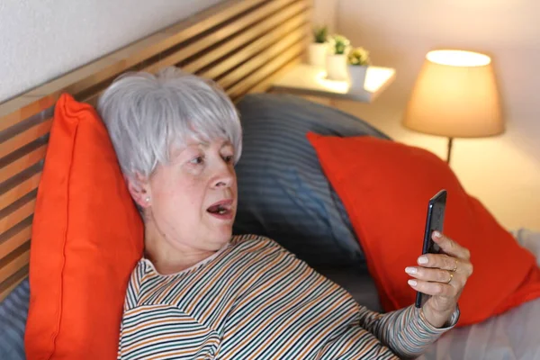Ώριμη Γκρίζα Μαλλιά Γυναίκα Χρησιμοποιώντας Smartphone Ενώ Χαλαρώνοντας Στο Κρεβάτι — Φωτογραφία Αρχείου