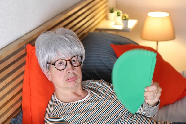 Dojrzała Siwowłosa Kobieta Zielonym Ręcznym Wentylatorem Relaksująca Się Łóżku Podczas — Zdjęcie stockowe