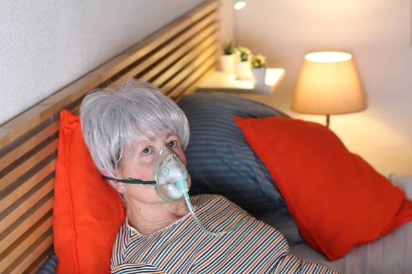 mature grey haired woman in oxygen mask while relaxing in bed during self isolation at home