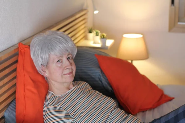 mature grey haired woman relaxing in bed during self isolation at home