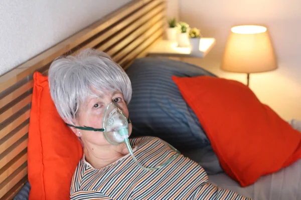 Ώριμη Γκρίζα Μαλλιά Γυναίκα Μάσκα Οξυγόνου Ενώ Χαλαρώνοντας Στο Κρεβάτι — Φωτογραφία Αρχείου