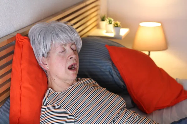 成熟的灰发女人在家里自我隔离时躺在床上打呵欠 — 图库照片