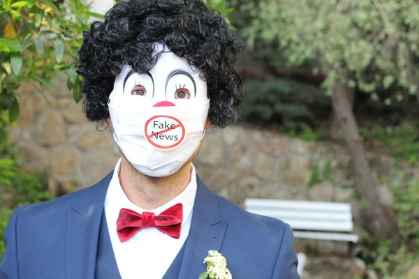 close-up portrait of groom in clown mask with covered mouth and fake news sticker standing in garden