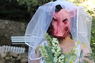 Gelinin korku maskeli portresi, gelin buketi ve yeşil bahçeli elbisesi.