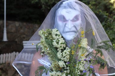 Gelinin korku maskeli portresi, gelin buketi ve yeşil bahçeli elbisesi.