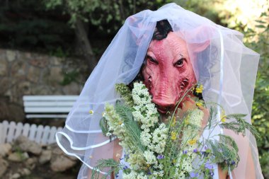 Gelinin korku maskeli portresi, gelin buketi ve yeşil bahçeli elbisesi.