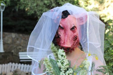 Gelinin korku maskeli portresi, gelin buketi ve yeşil bahçeli elbisesi.