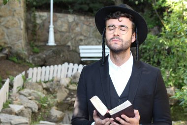 Geleneksel şapkalı yakışıklı hahamın doğal arka planda Tanakh ile yakın plan portresi.