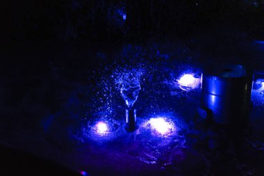 Damlalar çeşmeye saçılır mavi arka ışıklandırma ile geceleyin, yakın plan.