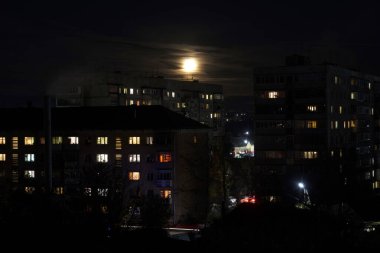 Evening view of Russian high-rise buildings with light in the windows, the moon shines from behind the clouds.
