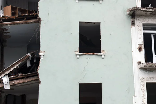 Wall of a destroyed house with glassless windows and insides, a dove on a cornice.