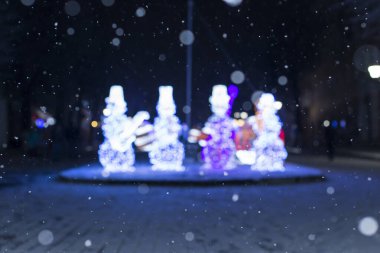 Bulanık festival arka planı, düşen kar ve Noel ve yeni yıl sokak dekorasyonu, parlayan kardan adam.
