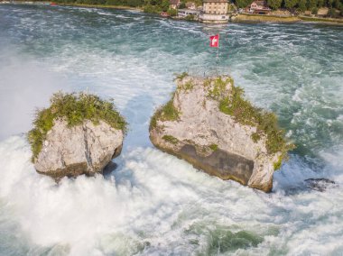 Ren nehrindeki kayaların hava manzarası İsviçre 'de İsviçre bayrağıyla Schaffhausen yakınlarında çağlayan suları gösteriyor.