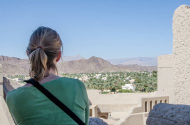 Girl looking across Bahla fort to mountains in Oman. 