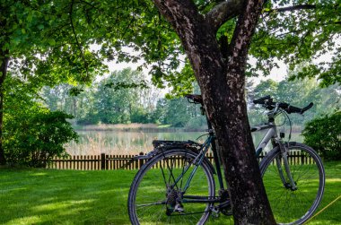 Romantik gölün önünde, yemyeşil ağaçların arasında bisiklet sürmek.