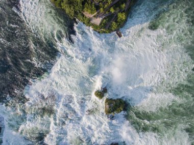 Ren nehrindeki kayaların hava manzarası İsviçre 'de İsviçre bayrağıyla Schaffhausen yakınlarında çağlayan suları gösteriyor.