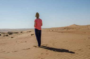 Girl standing alone in Wahiba sands desert looking at horizon