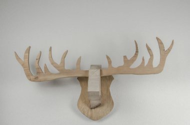 Beyaz duvarda asılı duran ahşap boynuz kupası, soyut hayvan heykeli.