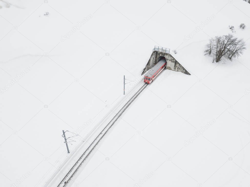 Aerial view of train in front of tunnel in winter landscape with snow in Swiss mountains