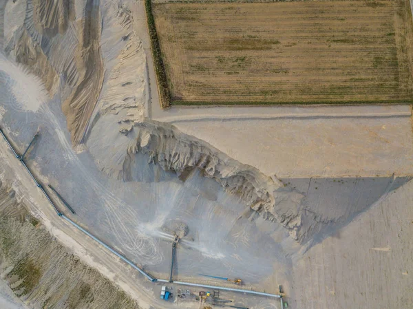 Aerial view of open cast gravel mine in Switzerland. Land grabbing for mining industry. Fields beside gravel quarry.