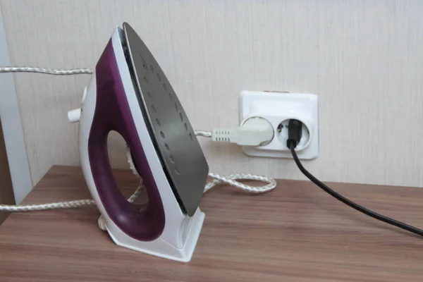 Una plancha eléctrica lila se coloca sobre una mesa conectada a una toma de pared — Foto de Stock