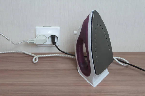 Duvar prizine takılmış bir masanın üzerinde leylak bir elektrikli ütü duruyor.
