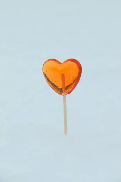Red heart shaped lollipop sticks out of snow in winter