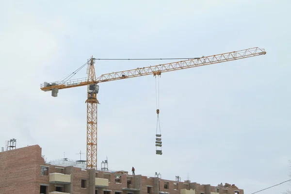 Turmdrehkran arbeitet auf Baustelle gegen den Himmel und ein Haus im Bau — Stockfoto