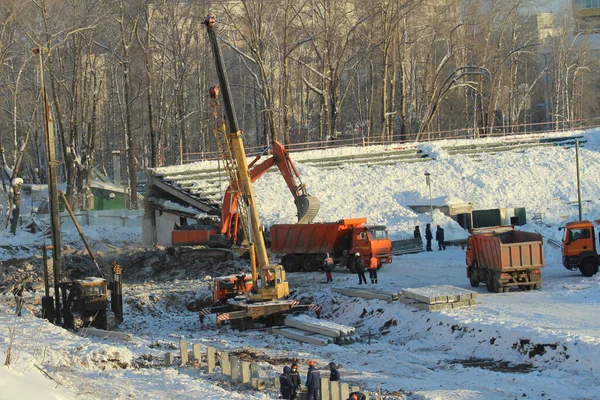 Excavator loads soil into a truck at a construction site and truck crane works at a construction site in winter in Russia — ストック写真