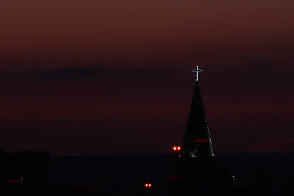 Glowing cross on the spire of a Babtist church at dusk against a sunset crimson sky over the horizon in the city of Syktyvkar in Russia — Stok fotoğraf