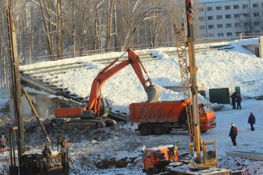 Excavator loads soil into a truck at a construction site in winter in Russia