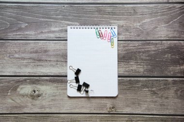 Raptiyeli ve ataçlı boş beyaz bir sayfa ve tahta tahtaların arka planında ataç olan not defteri..