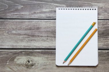 Tahta panoların arka planında basit grafit kalemle işaretleyici kağıdında boş beyaz bir sayfa bulunan bir not defteri var..