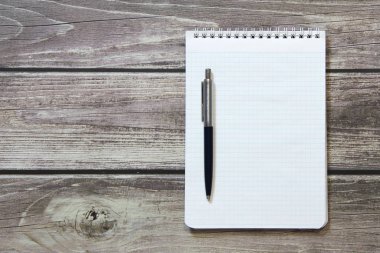 Notepad with a blank white sheet in a checker paper with ball pen lies on the background of wooden boards