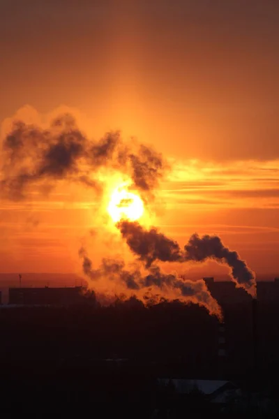 Red sun at sunset or dawn at dusk low above the horizon shrouded in smoke from the chimneys of the plant — Stockfoto