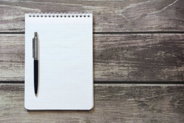 Notepad with a blank white sheet in a checker paper with ball pen lies on the background of wooden boards