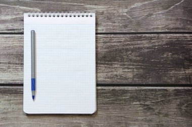 Notepad with a blank white sheet in a checker paper with ball pen lies on the background of wooden boards