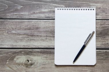 Notepad with a blank white sheet in a checker paper with ball pen lies on the background of wooden boards.
