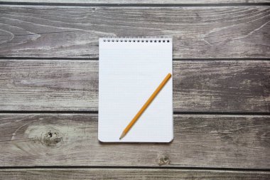 Tahta panoların arka planında basit grafit kalemle işaretleyici kağıdında boş beyaz bir sayfa bulunan bir not defteri var.