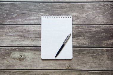 Notepad with a blank white sheet in a checker paper with ball pen lies on the background of wooden boards.