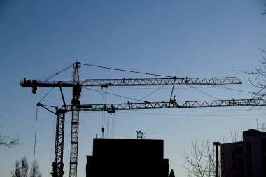 Gökyüzüne karşı bir inşaat alanında çalışan iki vinç ve inşaat halindeki bir ev. Endüstriyel inşaat. Metin ve tasarım için yer.
