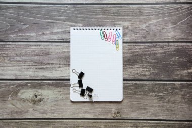 Raptiyeli ve ataçlı boş beyaz bir sayfa ve tahta tahtaların arka planında ataç olan not defteri.