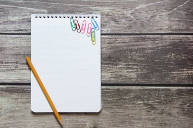 Dama kağıdında boş beyaz bir sayfa ve basit grafit kalem ve ataçlarla tahta tahtanın arka planında duran bir not defteri.