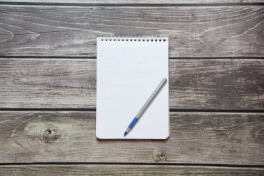 Notepad with a blank white sheet in a checker paper with ball pen lies on the background of wooden boards.